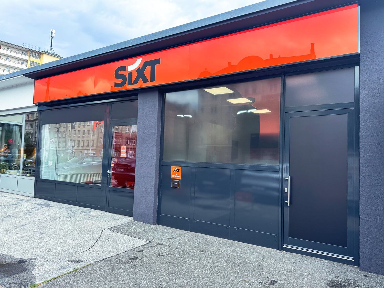 SIXT-Filiale mit orangefarbener Fassadenblende, schräg von der Seite