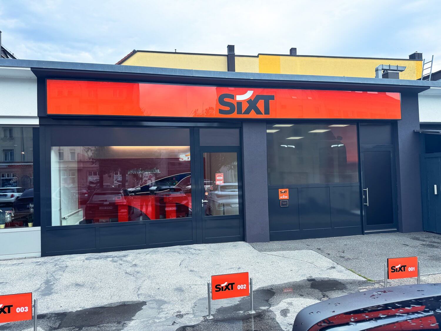 SIXT-Filiale mit nummerierten Parkplatzschildern vor der Fensterfront